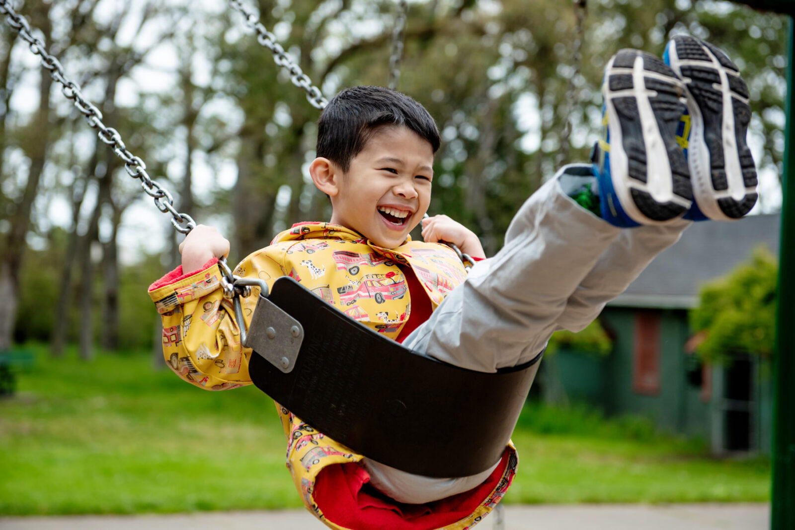 A happy child wearing a yellow jacket is smiling as he plays on the swings at the Beacon Hill Park play area.