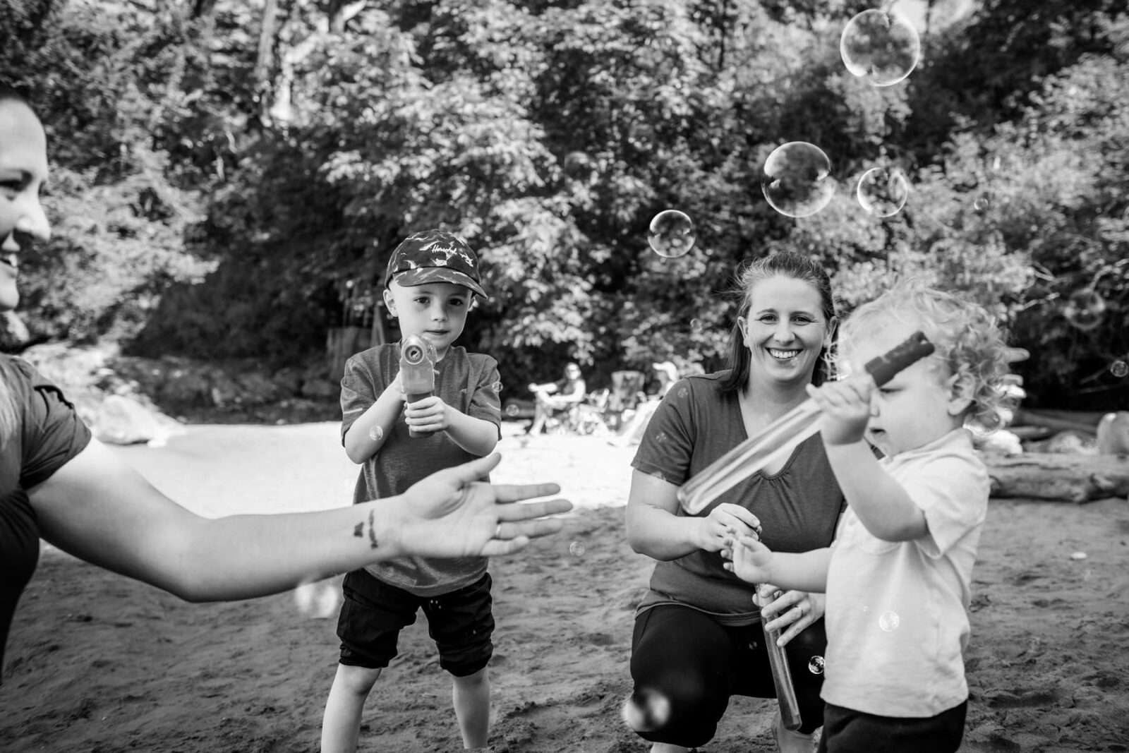 A family of two moms and two boys playing at the beach with bubbles at Hollydene park in victoria bc