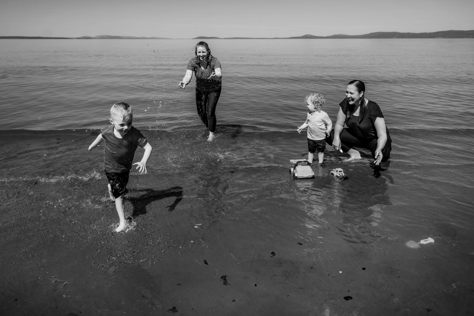 A family of four playing at Holydene beach in Victoria BC at low tide - photographed in Black and White by documentary photographer Christina Craft.