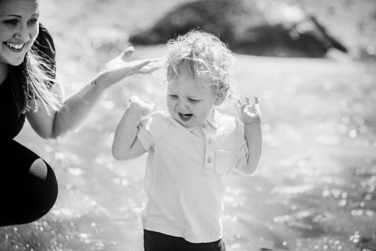 A candid happy photo of a blonde boy playing with a smile on his face at the beach with his mom in Victoria BC.