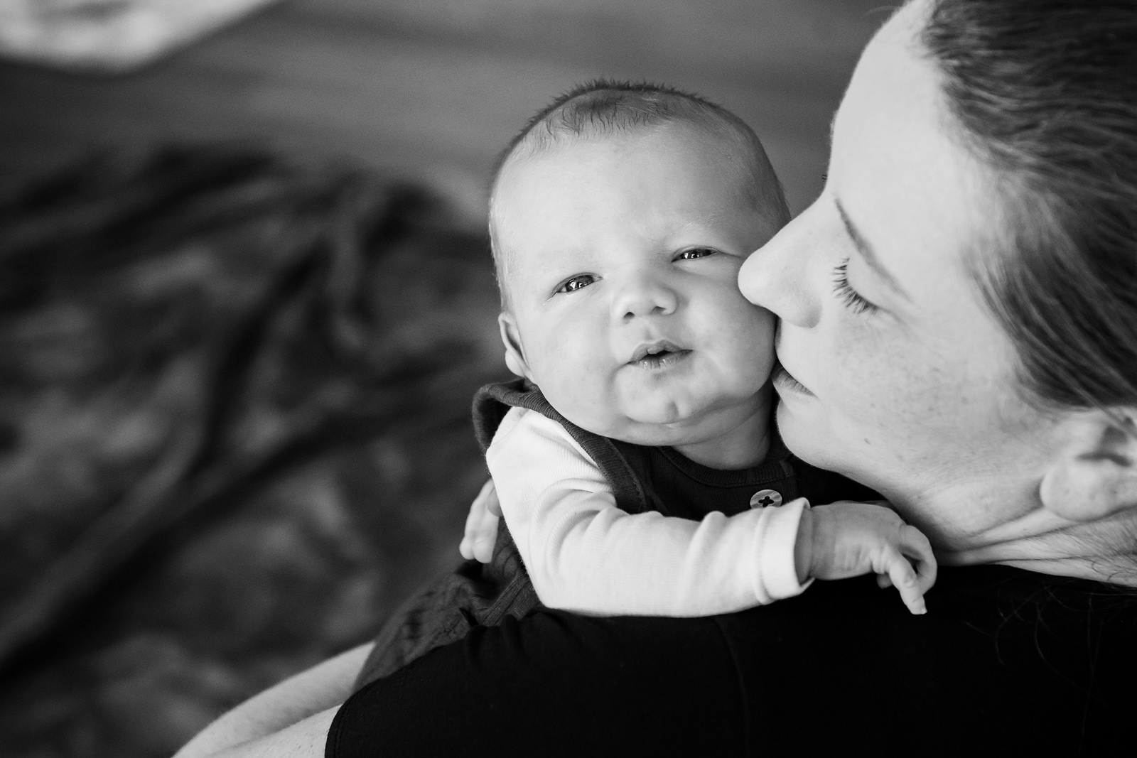 A black and white professional newborn portrait of a mother holding her newborn baby. The baby is looking at the camera.