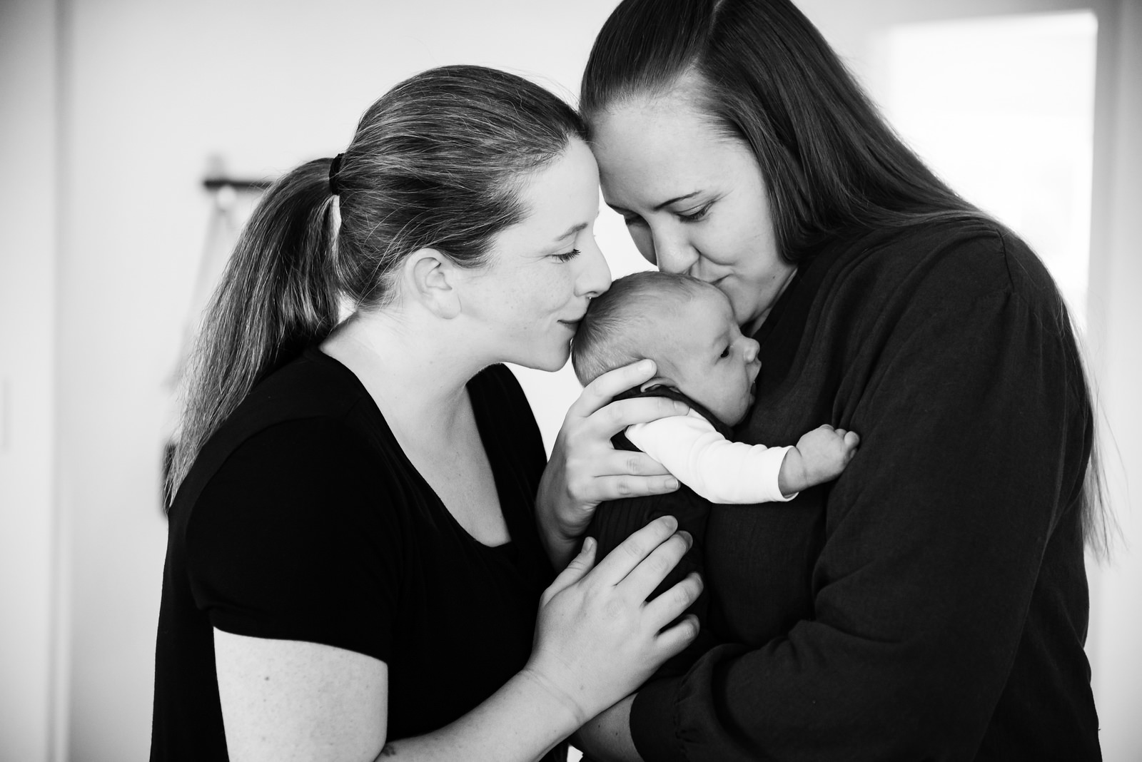 Two moms kissing their newborn baby in a natural and candid newborn photo.