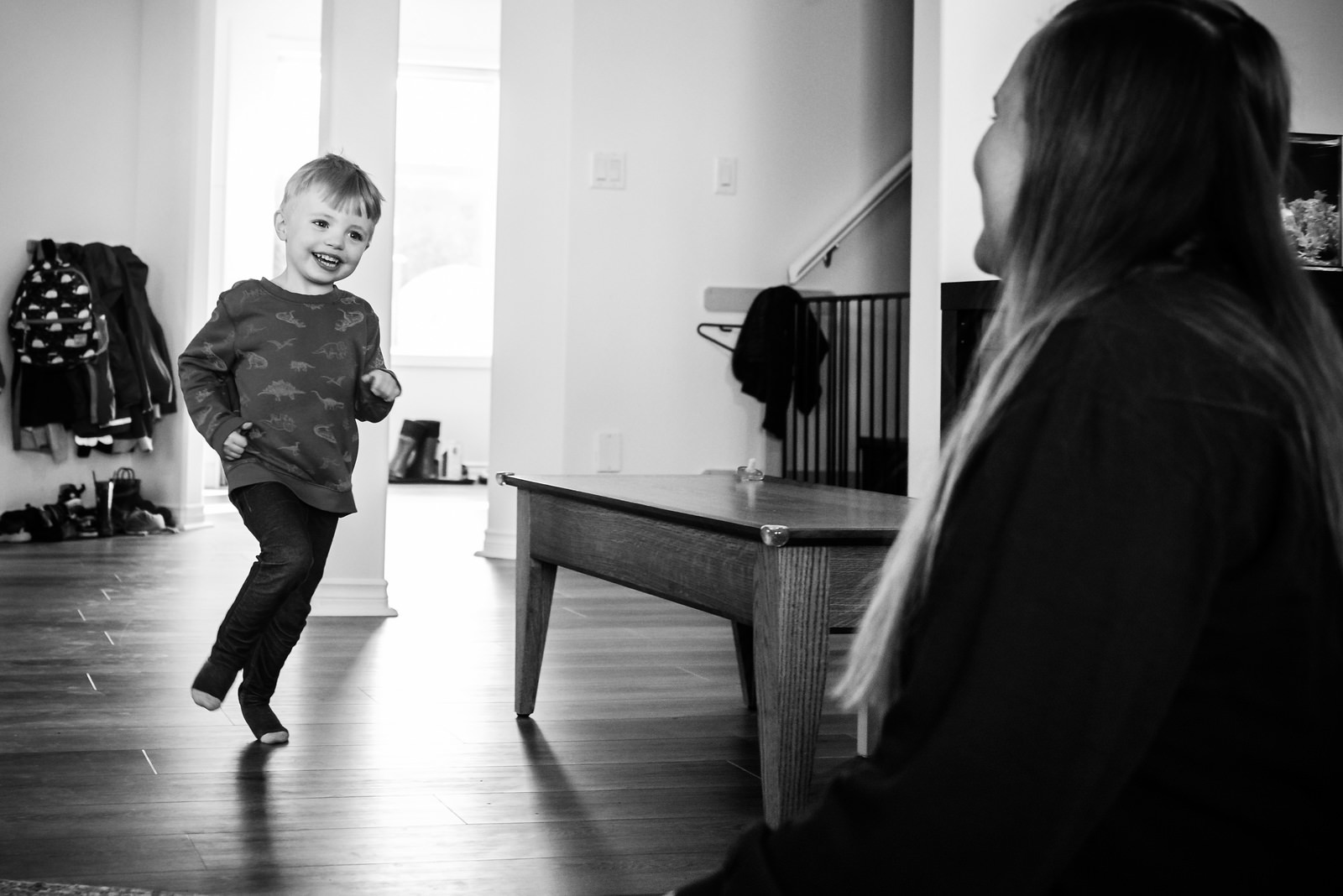 A black and white documentary family photo of a young boy running into the living room with a smile on his face.