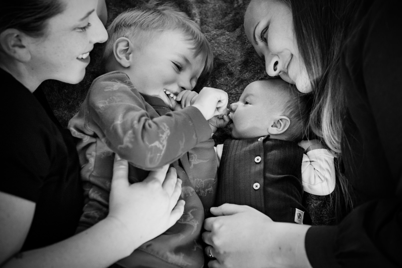 A cuddly candid newborn baby portrait with two moms holding their children and smiling.