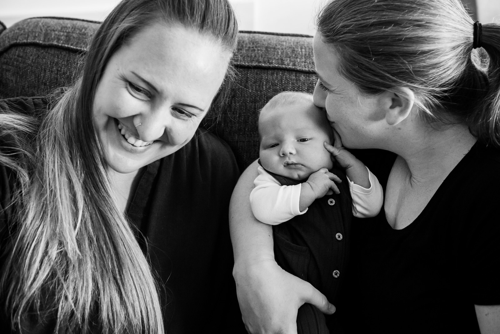 Moms enjoying a cuddle and kissing their newborn baby in their living room in Victoria BC