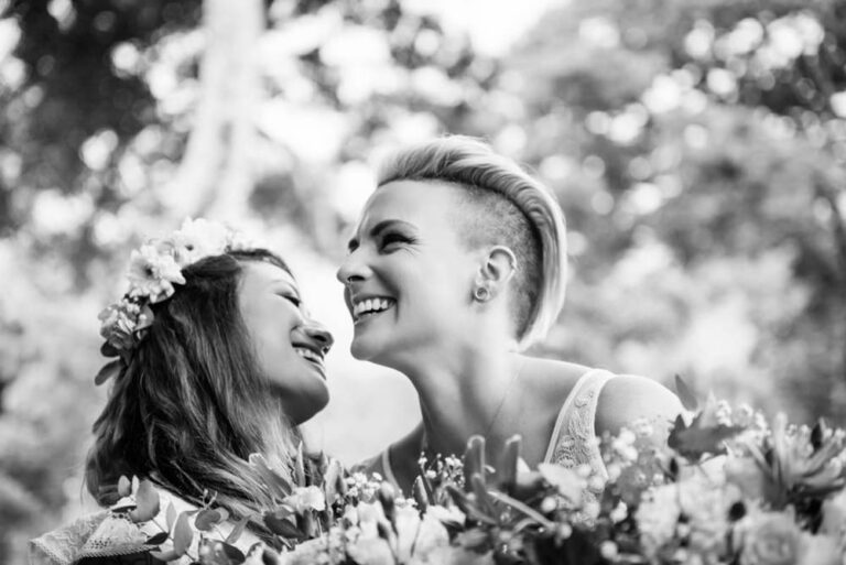 Wedding couple (LGBTQ2S+) in black and white who are laughing with joy because they just saw each other for the first time. The image is a closeup in Victoria BC and it's in Black and White.