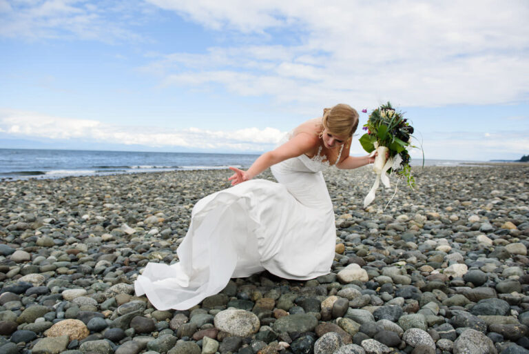 A candid colour photo of a bride on a beach in Vancouver Island with her dress blowing in the air.