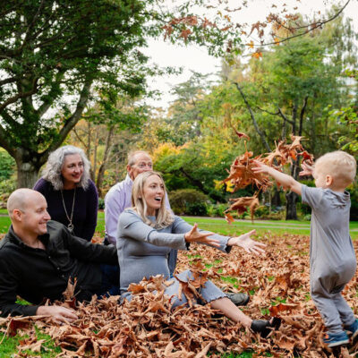 A two year old boy throws fall leaves at his parents and grandparents at Beacon Hill Park in Victoria BC