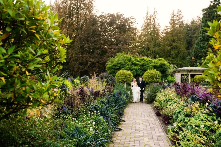 A bride and groom walks along the fall gardens in front of Hatley Castle among some of the ruins. This is a candid photo of the couple enjoying a brief moment before the reception.