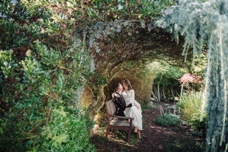 Victoria BC Backyard wedding Analog Film photography of a couple sitting on a bench surrounded by bushes on a warm day in October.