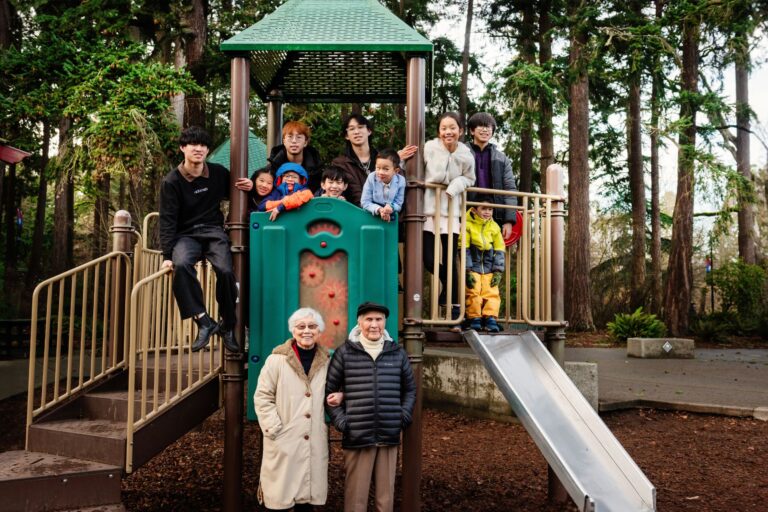 Grandparents stand in front of the slides at Beacon Hill Park in Victoria BC with all of their grandchildren in the background.